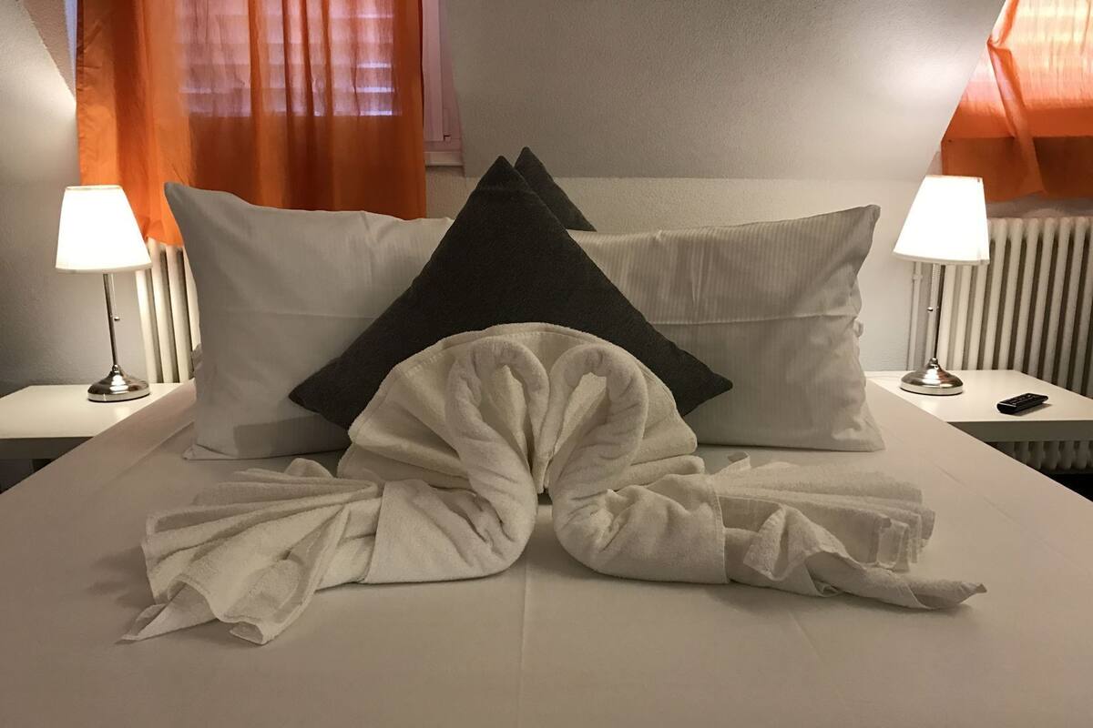 A neatly made bed with pillows, a blanket, and a remote control on a nightstand.