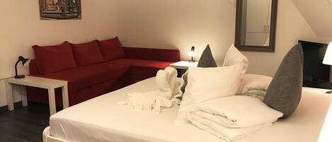 Una habitación de hotel con una cama, un sofá rojo, una mesita de noche con una lámpara y un cuadro en la pared.
