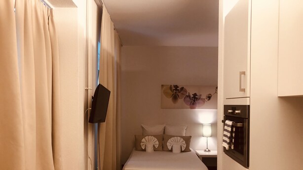 A compact bedroom with a bed, a bedside table, a lamp, and a flat-screen TV mounted on the wall. - INSIDE FIVE City Apartments (Zürich)