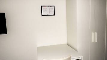Une petite pièce blanche, avec un bureau et une chaise, une armoire blanche et un avis encadré accroché au mur.