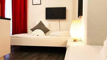 Et moderne hotelværelse med en seng, et natbord med lampe, et fladskærms-tv på væggen og en rød gardin.