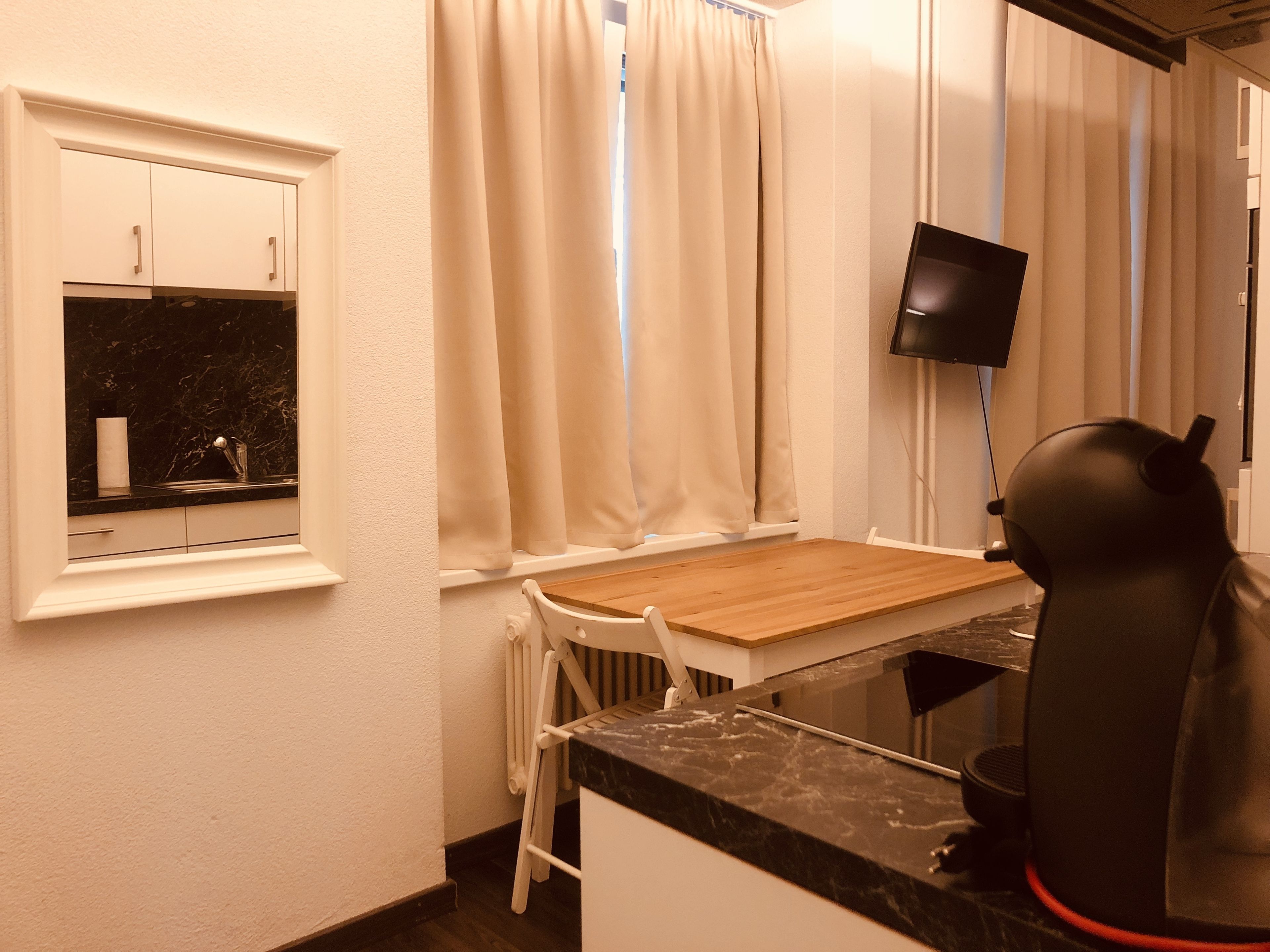 A small kitchenette with a wooden table, a sink, and a black speaker.