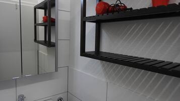 A bathroom with a mirror, a sink, and two black shelves with red objects on them.