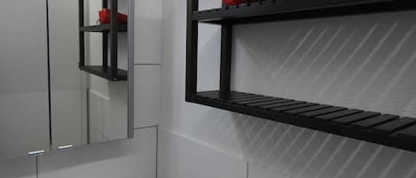 A bathroom with a mirror, a sink, and two black shelves with red objects on them.