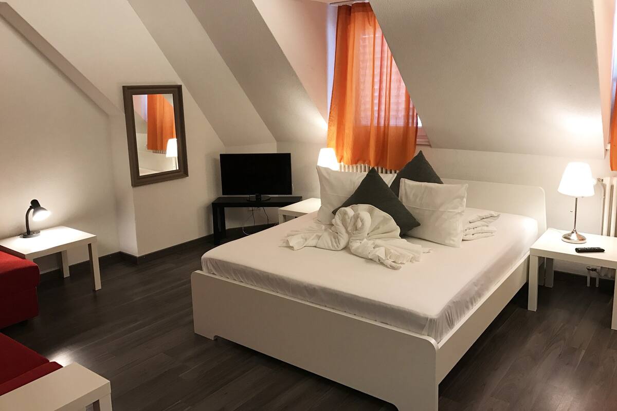 A modern hotel room with a large bed, a flat-screen TV, a desk, and a red chair.