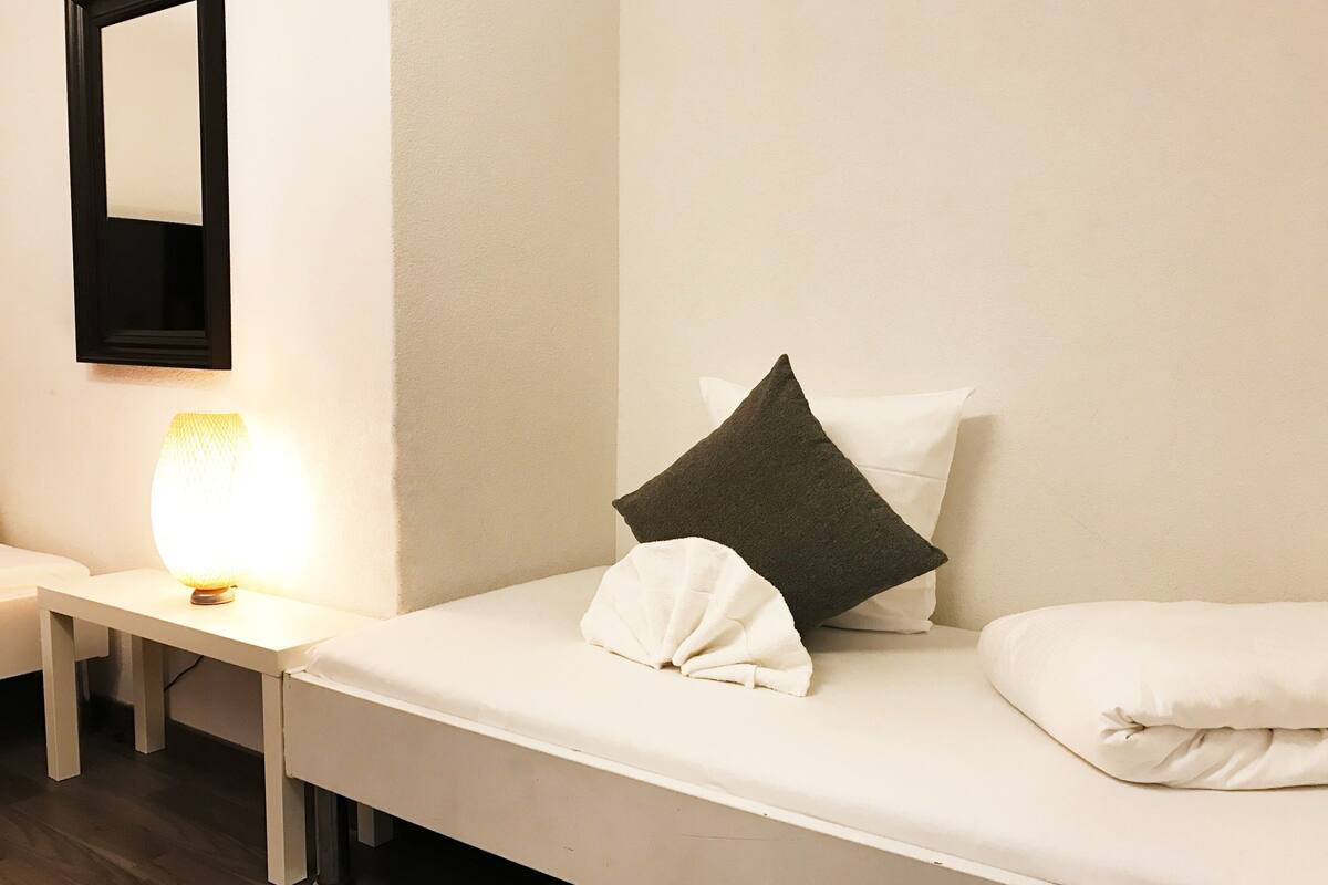 A neatly made bed with pillows, a bedside table with a lamp, and a mirror on the wall.