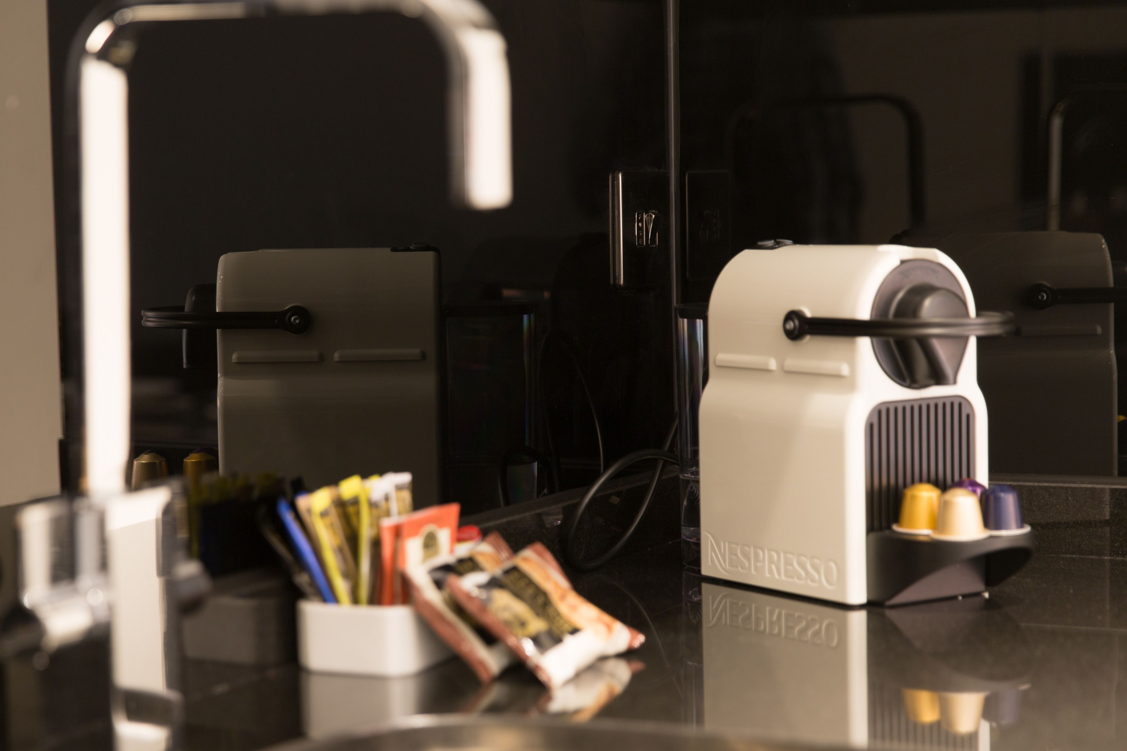 A coffee machine with a cup holder, a magazine holder, and a small stack of magazines on a reflective surface.