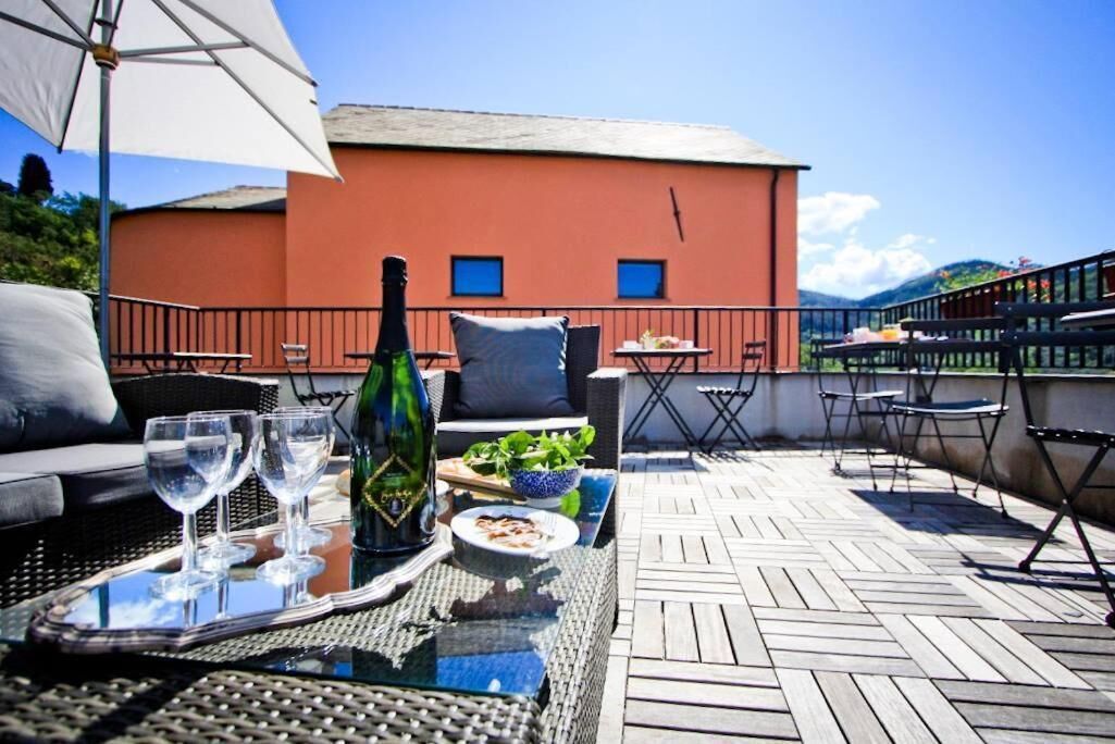 A terrace with outdoor furniture, a table with a bottle and glasses, and a view of a red building.