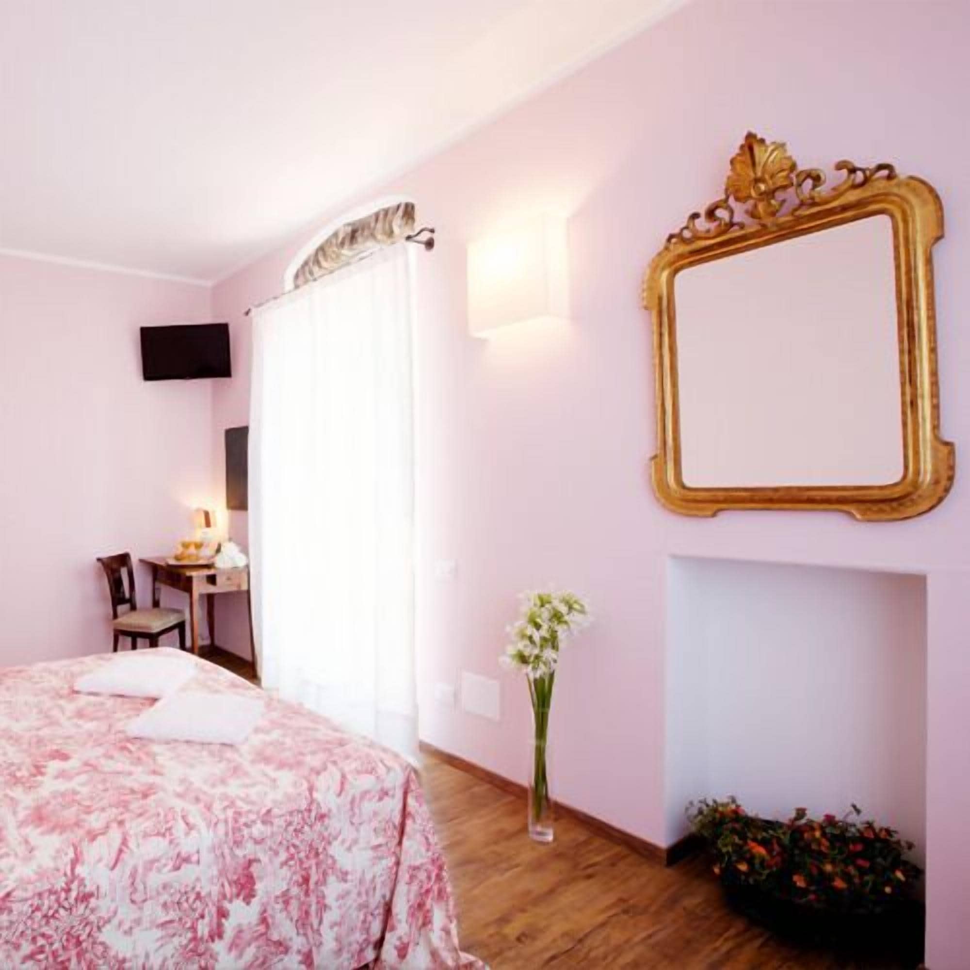 Una camera da letto con un letto, una scrivania, una sedia, uno specchio e un vaso con fiori.