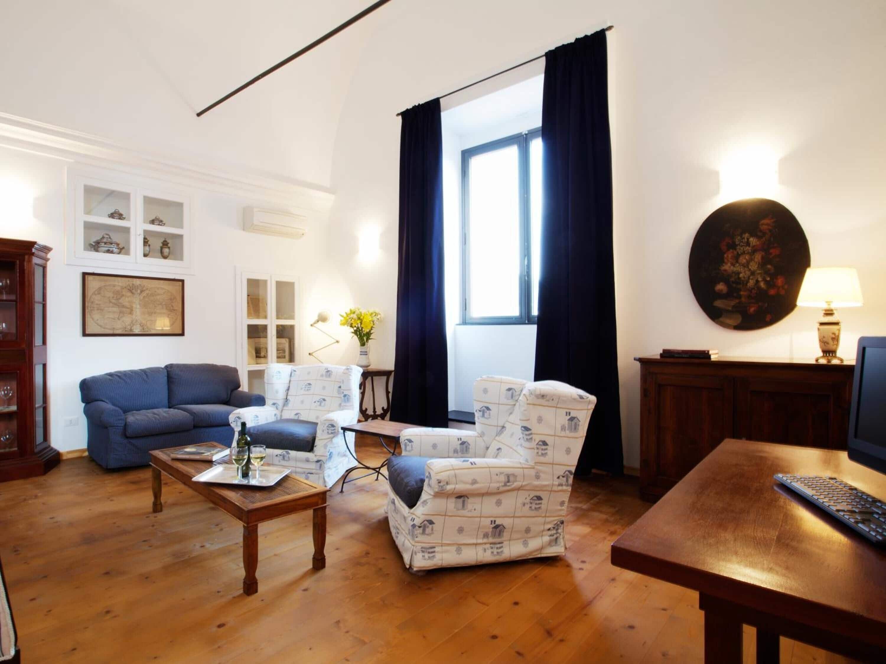Una sala de estar con un sofá azul, sillones estampados, una mesa de centro de madera y un televisor sobre un mueble de madera.