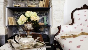 A room with a fireplace, a bookshelf, a table with a teapot and cups, and a patterned armchair. - La Madonetta - Dimora d'epoca - (Levanto)
