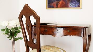 A wooden desk with a chair, a vase with flowers, and a painting on the wall.