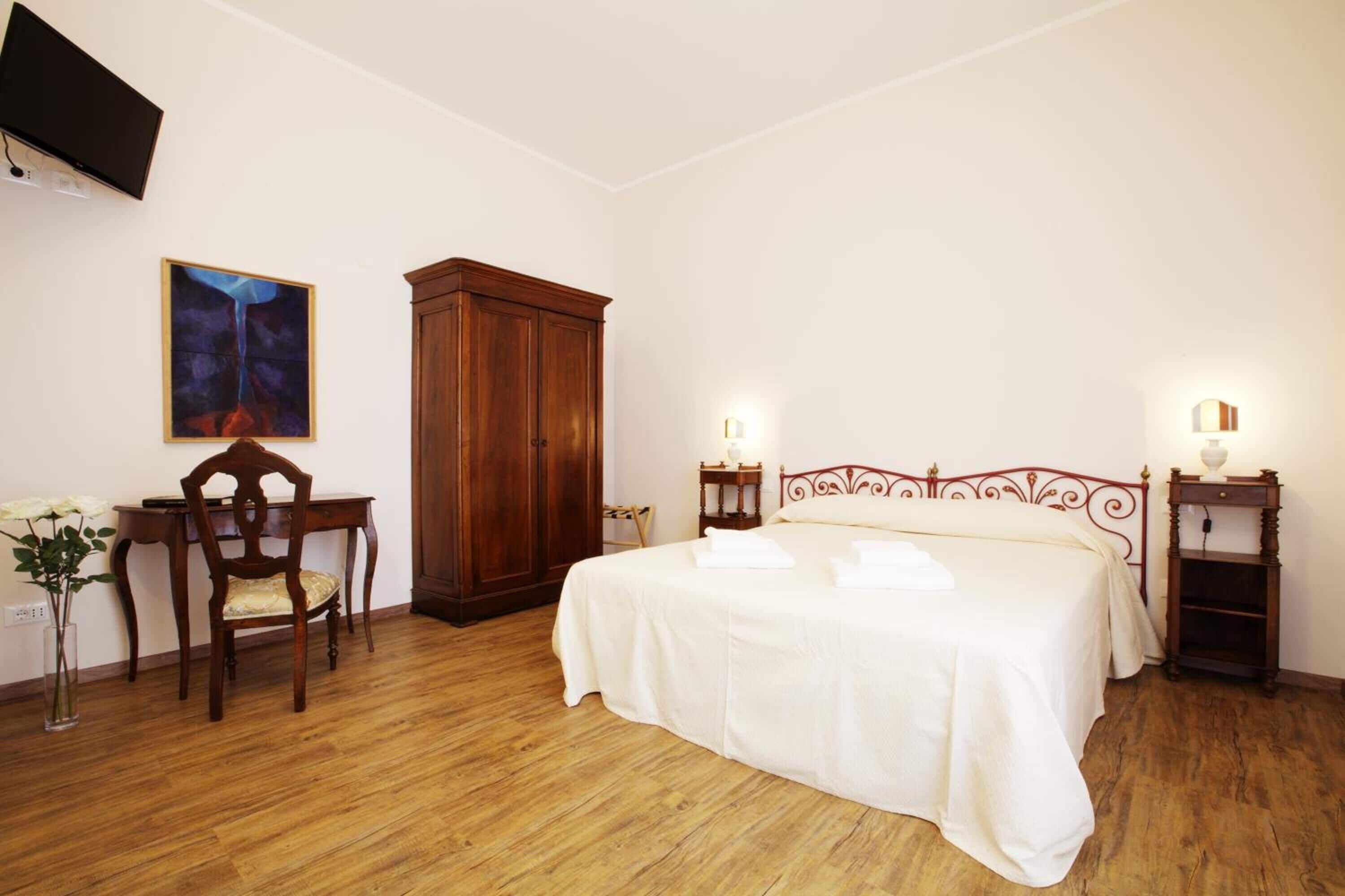 Ein Schlafzimmer mit einem hölzernen Bett, einem Schrank aus Holz, einem Schreibtisch, einem Stuhl, einem an der Wand montierten Fernseher und einem Gemälde.