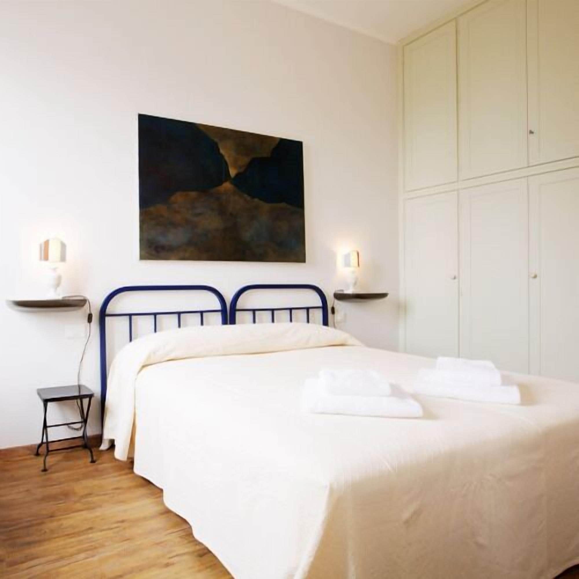 A bedroom with a bed, bedside tables, a painting, and a wardrobe.