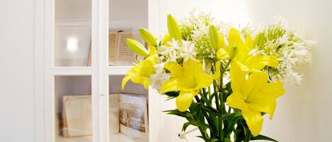A white cabinet with glass doors containing books and a white vase with yellow and white flowers.