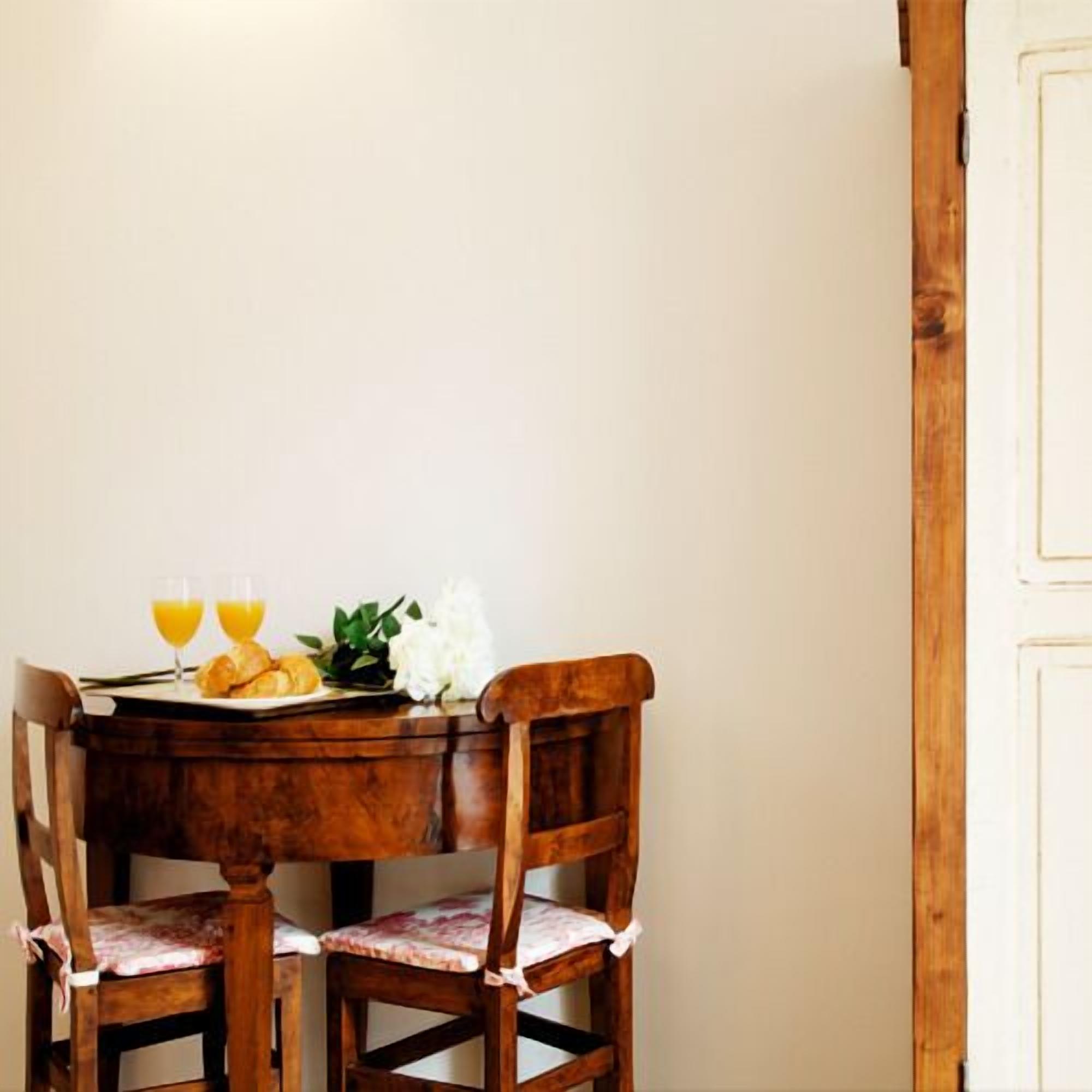 Una mesa de madera con dos sillas, un plato con cruasanes y jugo de naranja, y un arreglo floral blanco.