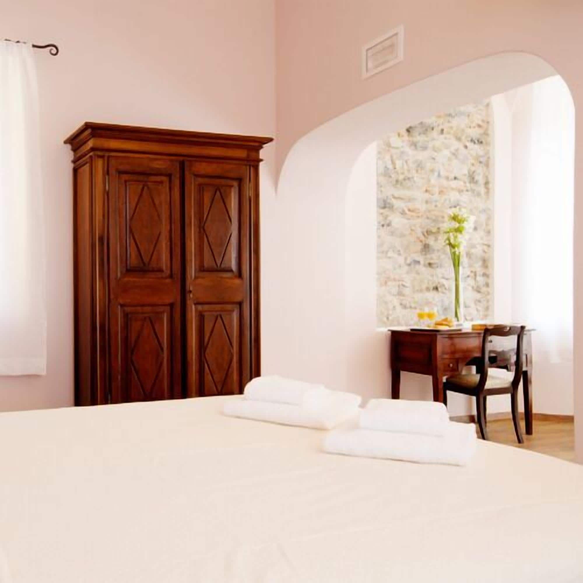 A hotel room with a large bed, a wooden wardrobe, a desk with a chair, and a decorative wall.