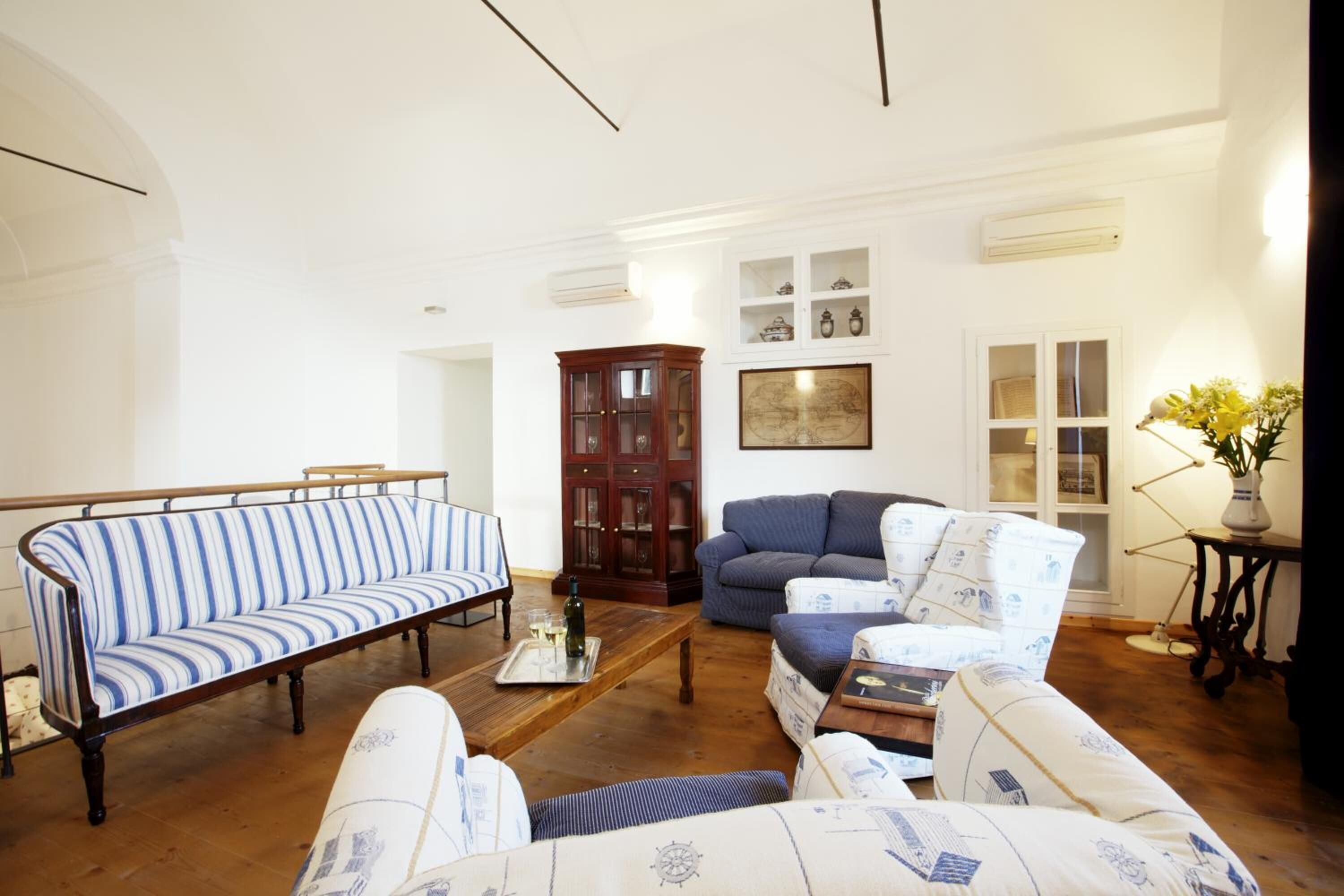 A living room with a striped sofa, a blue armchair, and a patterned armchair. There is a wooden cabinet and a framed map on the wall.