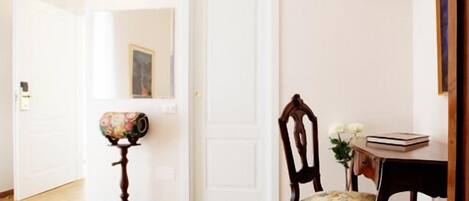 Una habitación con suelo de madera, un escritorio con una silla, un televisor montado en la pared y una puerta con espejo.