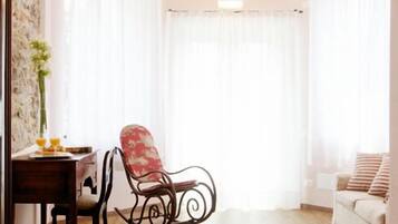 A cozy living room with a wooden floor, a dining table with chairs, a red upholstered chair, and a white sofa.