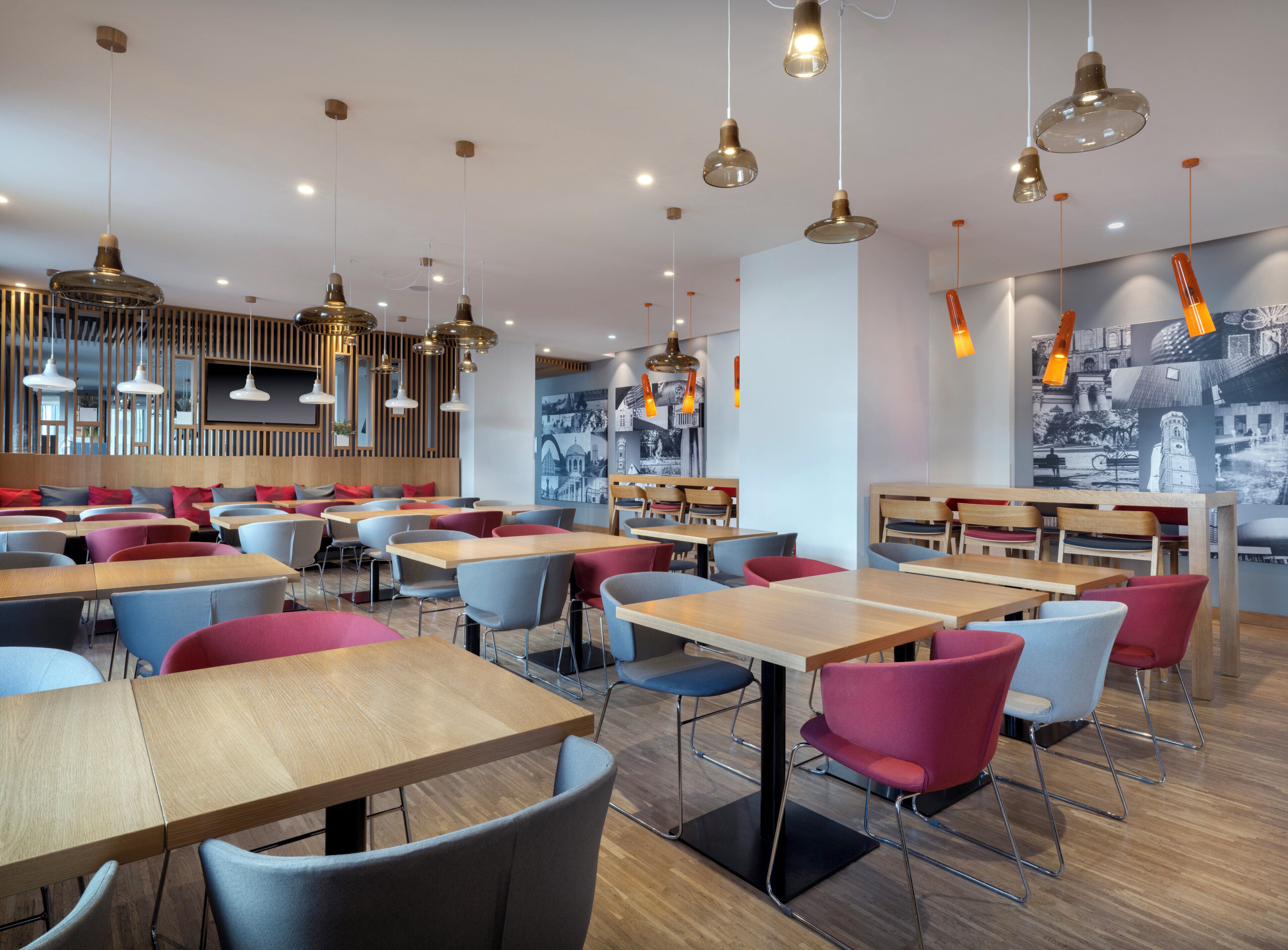 Een modern restaurantinterieur met houten tafels en stoelen, hanglampen en een muurschildering.