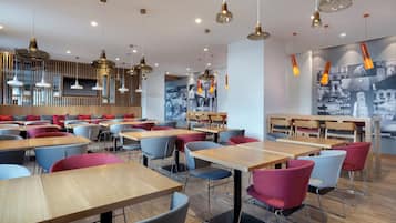 Een modern restaurantinterieur met houten tafels en stoelen, hanglampen en een muurschildering.