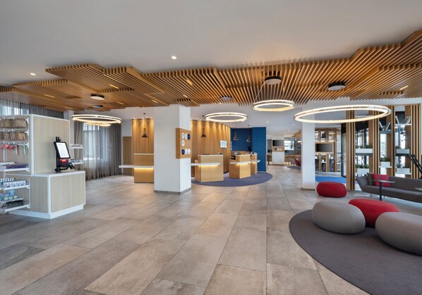 A modern hotel lobby with a reception desk, seating areas, and a large window offering a view of the outdoors. - Holiday Inn Express Munich City West by IHG (Munich)