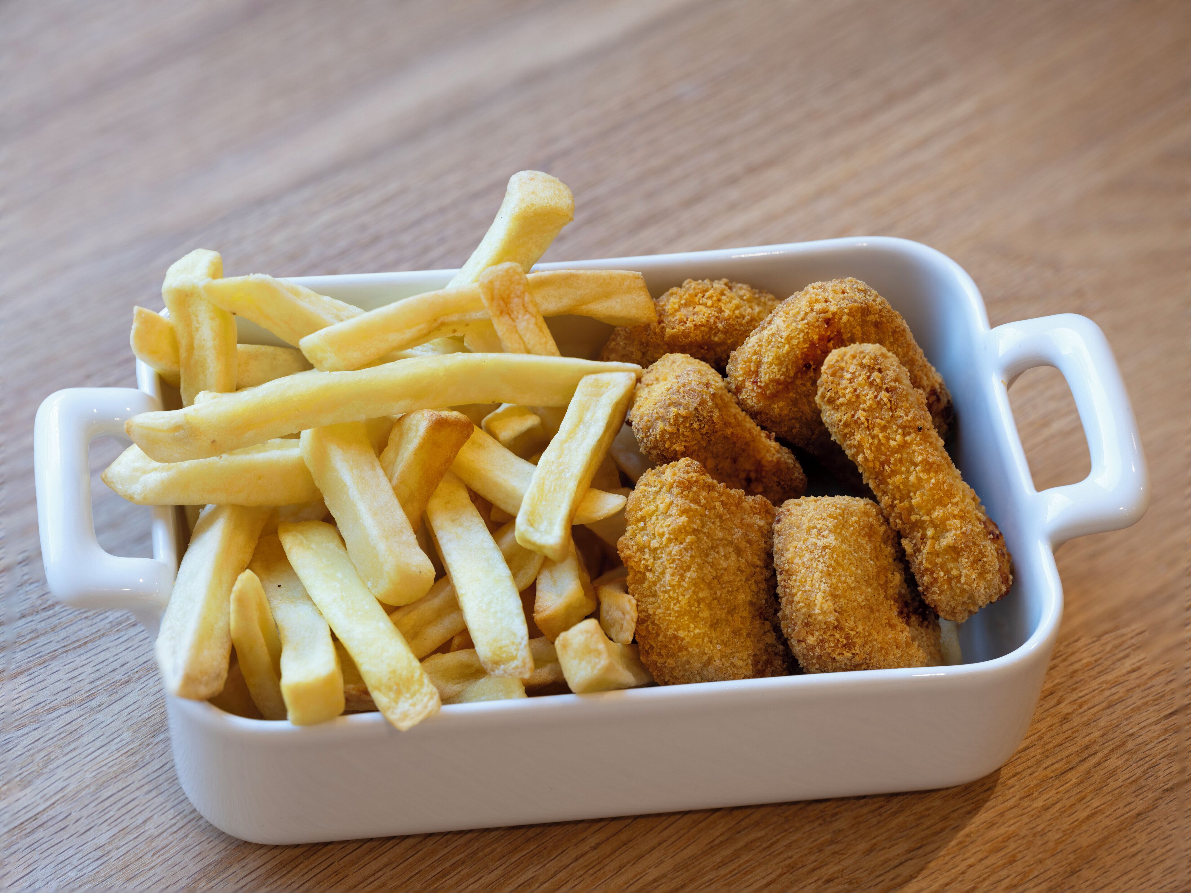 Un plat en céramique blanche contenant des frites et des morceaux de poulet pané, posé sur une table en bois.