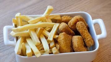 Un plato de cerámica blanca con papas fritas y tiras de pollo empanizado sobre una mesa de madera.