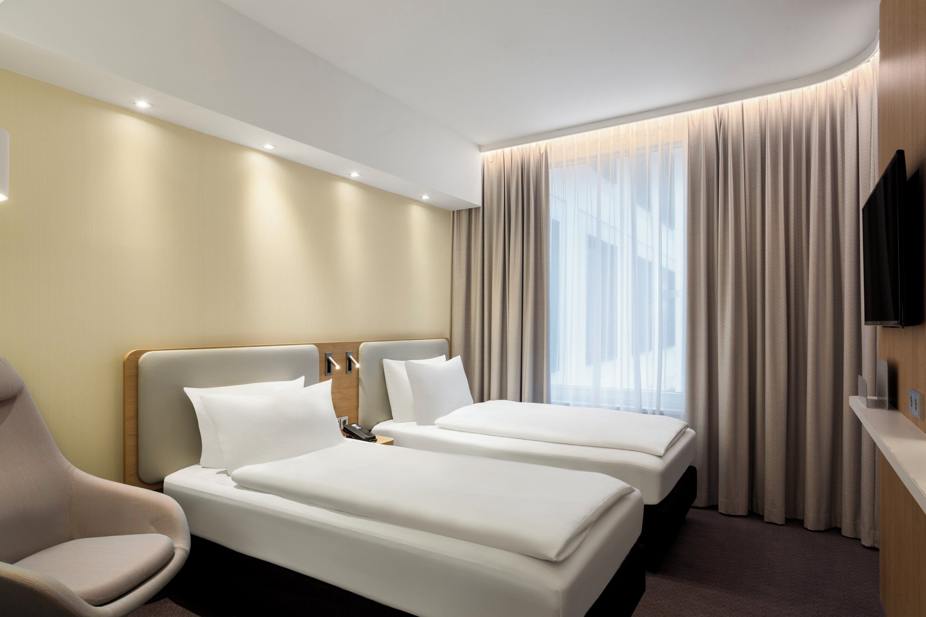 Habitación de hotel con dos camas, una silla, un televisor y una ventana con cortinas.
