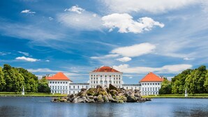 A large, symmetrical building with a central tower and two wings, surrounded by a body of water and greenery. - Holiday Inn Express Munich City West by IHG (Munich)