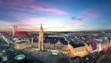 A historic city square with prominent Gothic architecture, including a tall clock tower and a cathedral with a red roof.