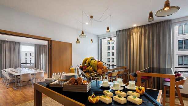 A hotel room with a dining area featuring a buffet with fruits, pastries, and desserts. - Holiday Inn Express Munich City West by IHG (Munich)