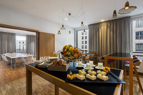 A hotel room with a dining area featuring a buffet with fruits, pastries, and desserts. - Holiday Inn Express Munich City West by IHG (Munich)