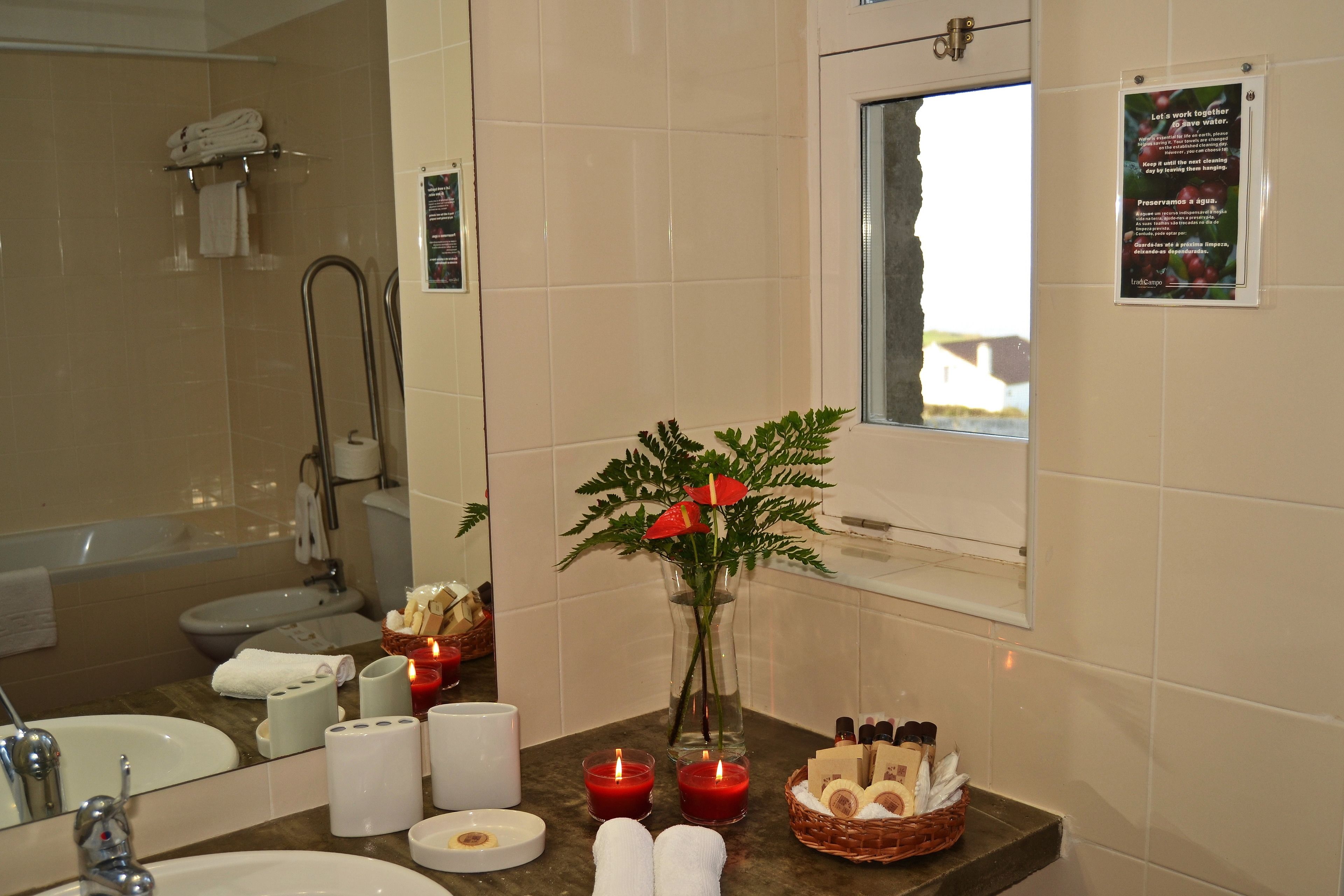 A bathroom with a bathtub, sink, and mirror. There are towels, candles, and a vase with flowers on the counter.