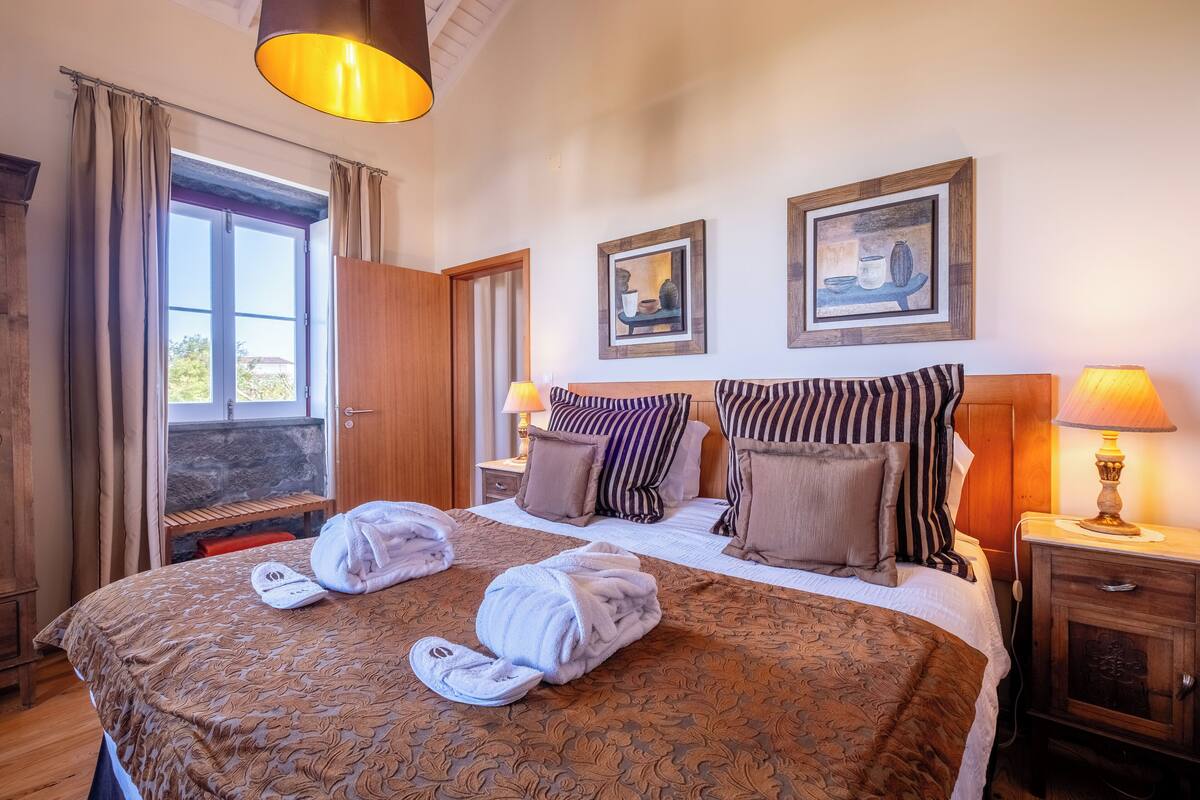 Ein Hotelzimmer mit einem großen Bett, zwei Nachttischlampen, einem Holznachttisch, einem Kleiderschrank und einem Fenster mit Vorhängen.