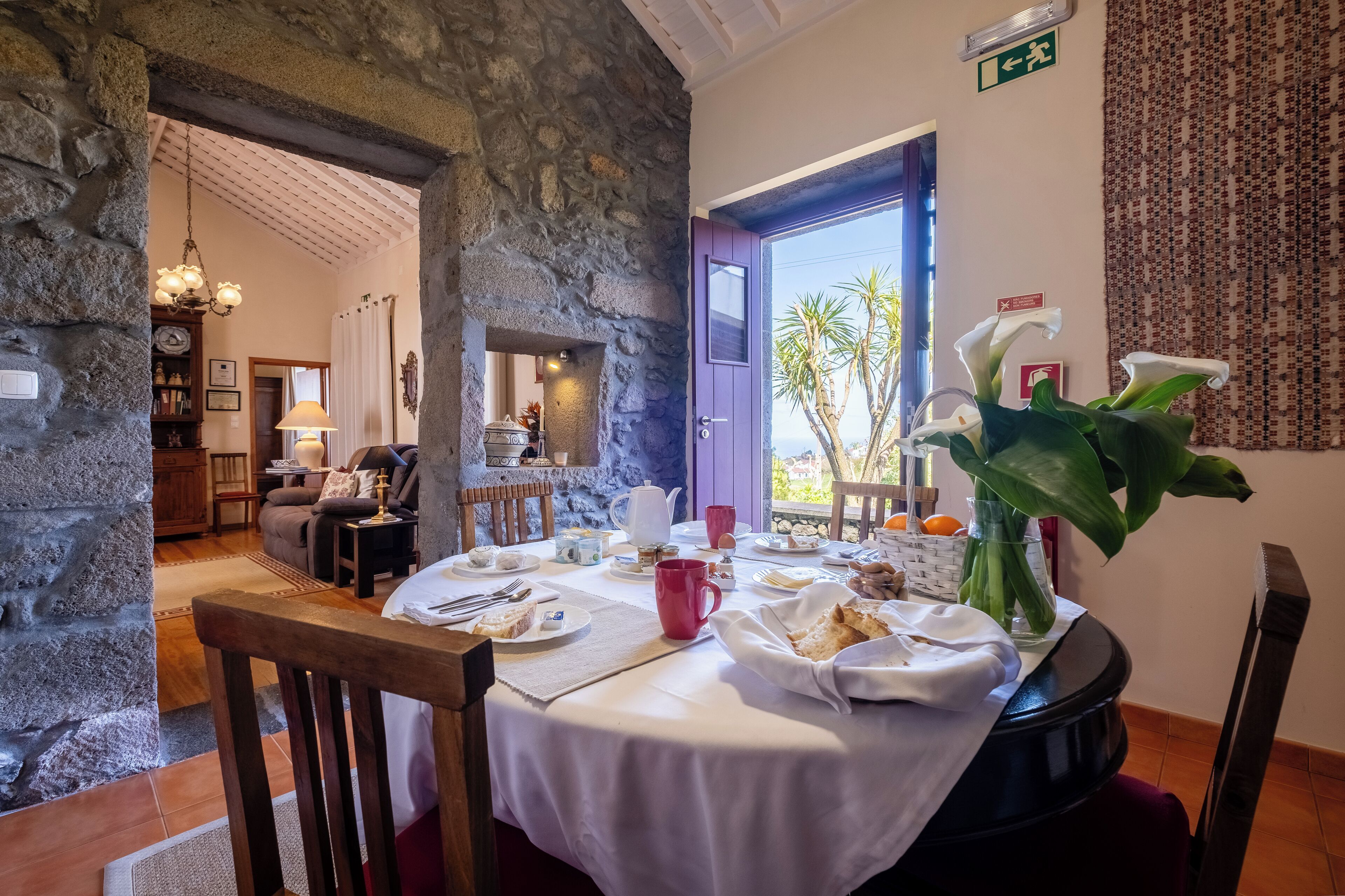 A dining area with a stone wall, a table set for breakfast, and a view of the outdoors.