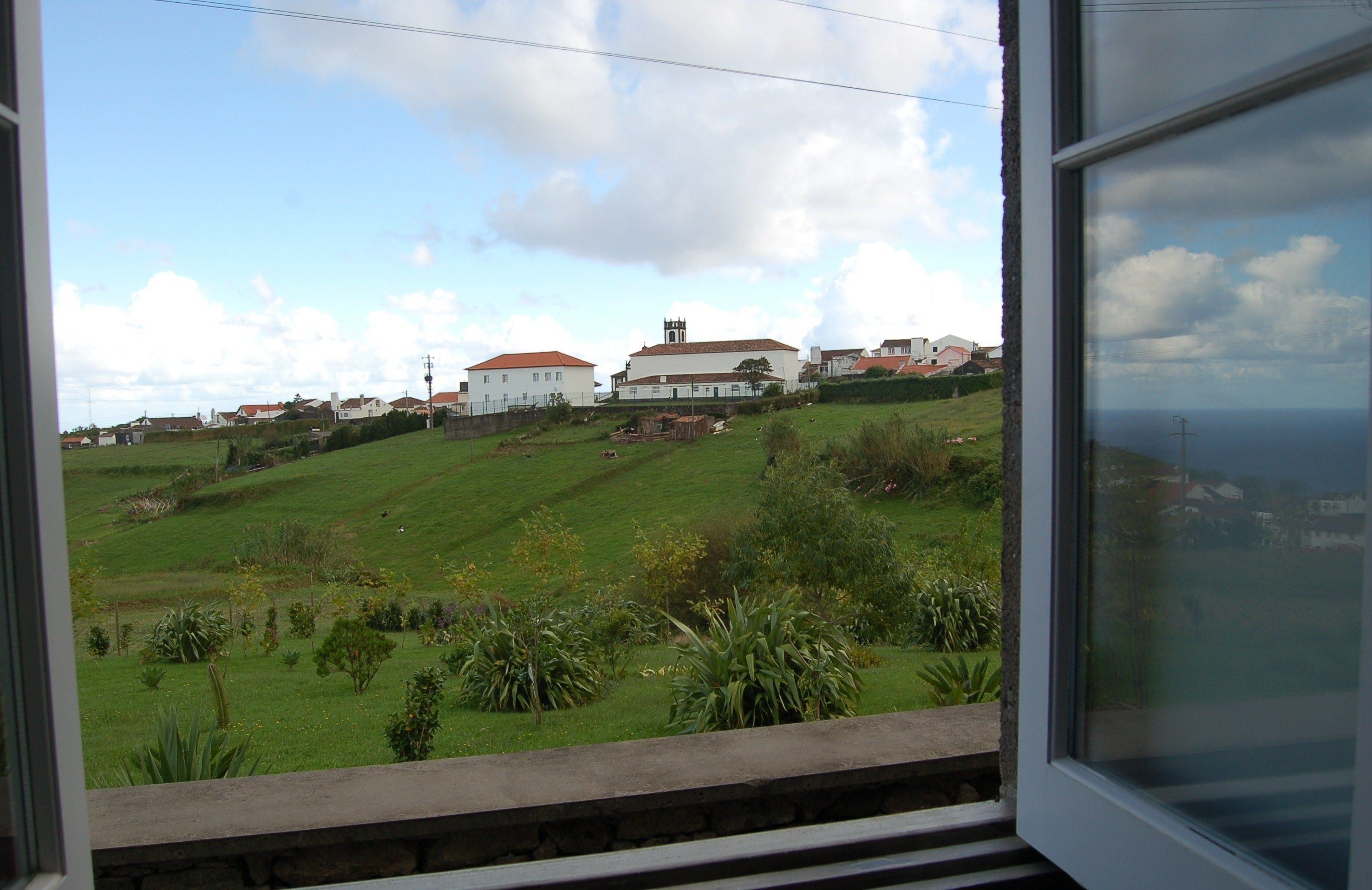 A view from a window overlooking a green landscape with buildings in the distance.
