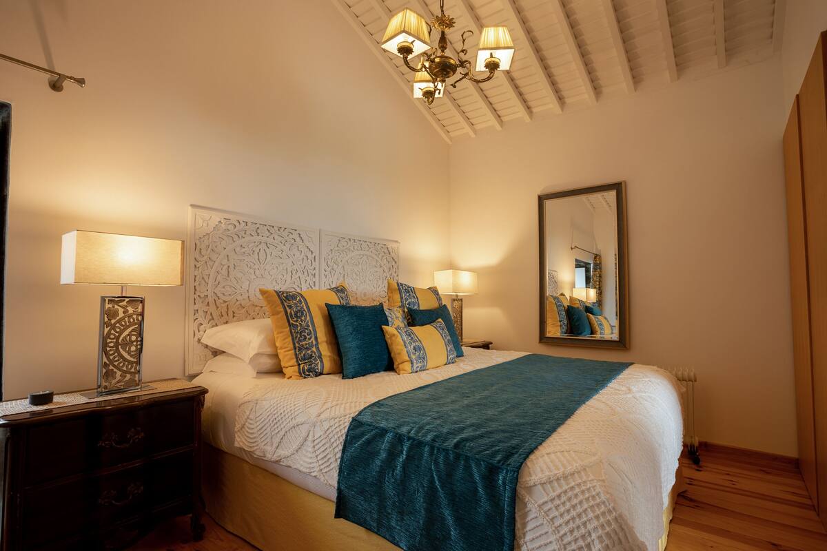 Ein Schlafzimmer mit einem großen Bett, zwei Nachttischen, einer Kronleuchter, einem Spiegel und einem Holzboden.