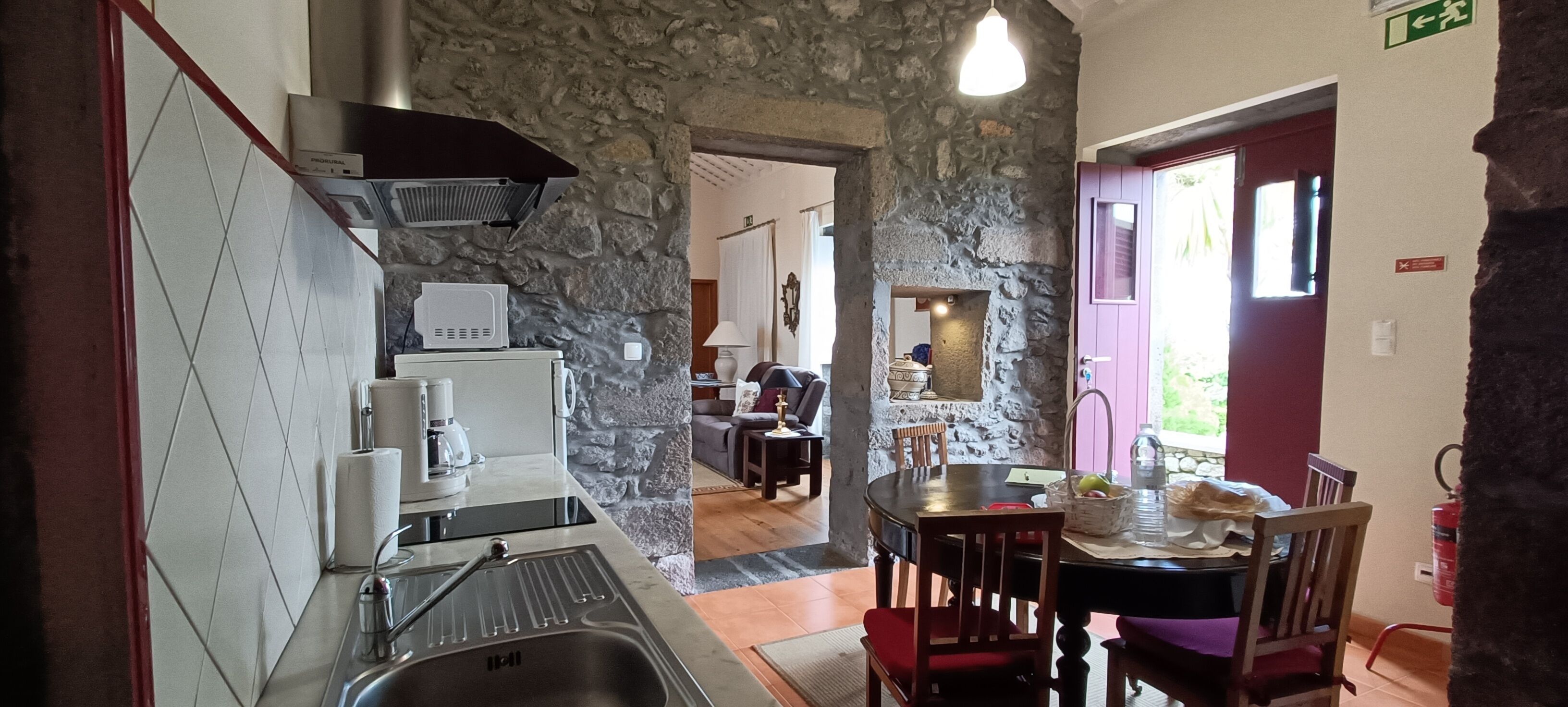 A kitchen with stone walls, a dining area with a table and chairs, and a visible exit sign.