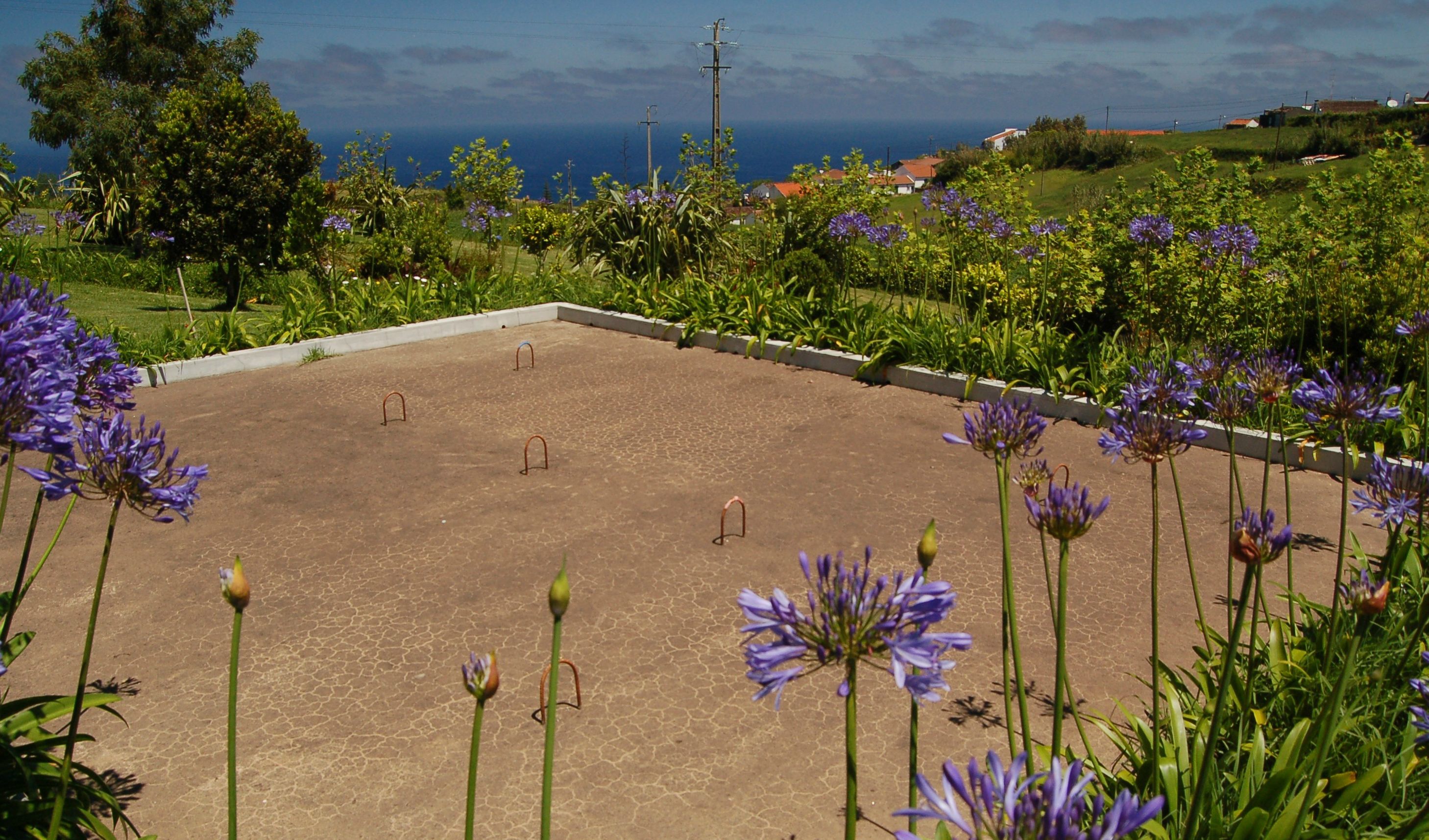 A square courtyard with a paved floor, surrounded by lush greenery and purple flowers.