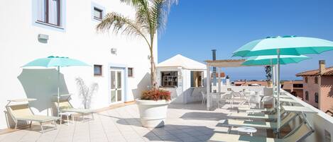 A rooftop terrace with sun loungers, umbrellas, and a potted plant.