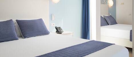 A hotel room with a bed, a bedside table with a phone, and a mirror reflecting the room.