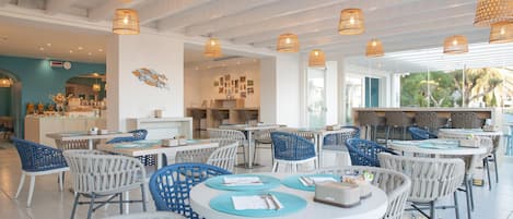 A spacious restaurant with round tables, blue and white chairs, and hanging wicker lamps.