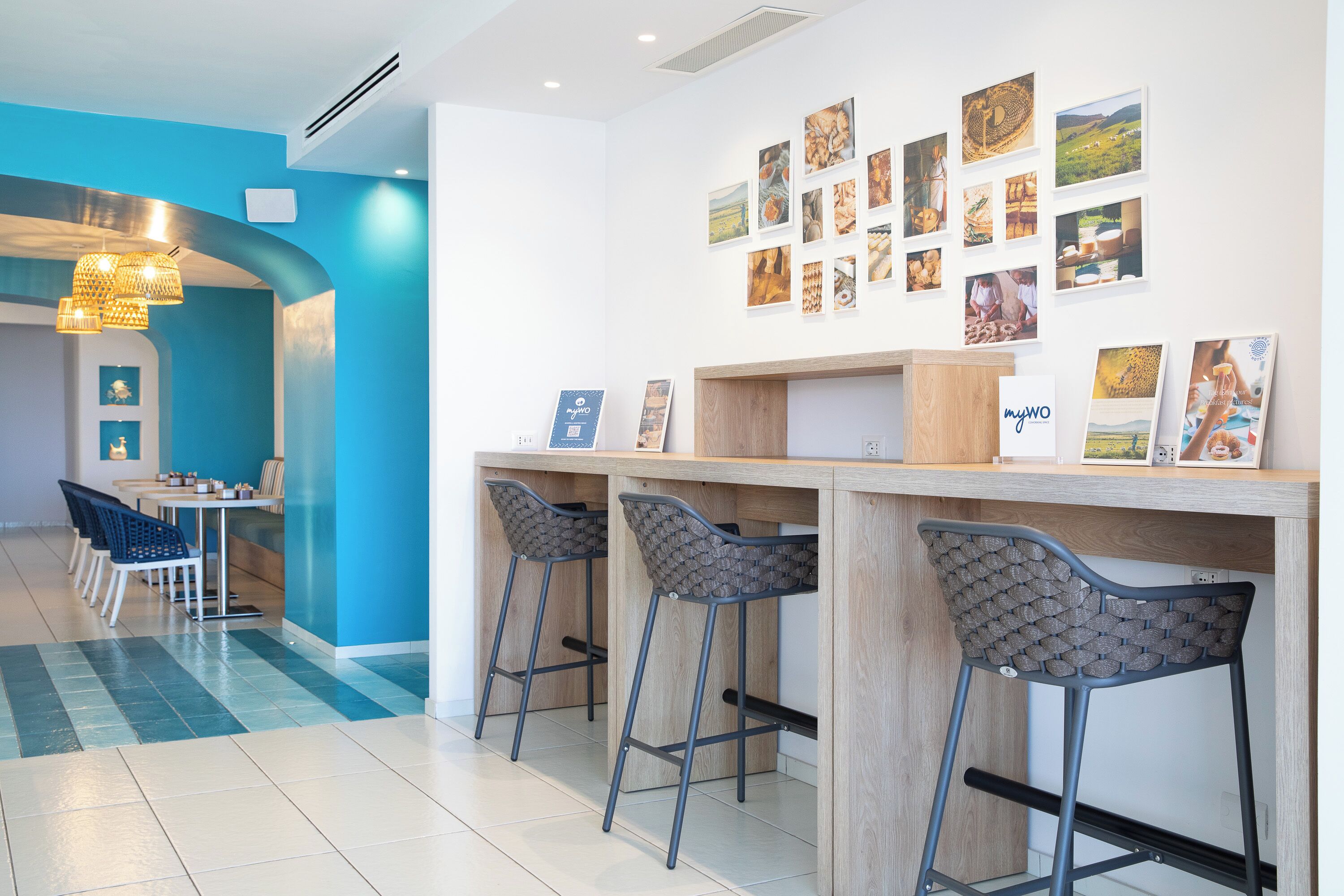Un'area bar moderna con sgabelli alti, un bancone in legno e una parete decorata con quadri.