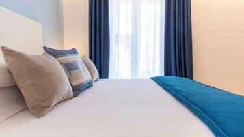 Una cama bien hecha con una colcha blanco y aguamarina, dos almohadas color beige y una almohada decorativa azul.