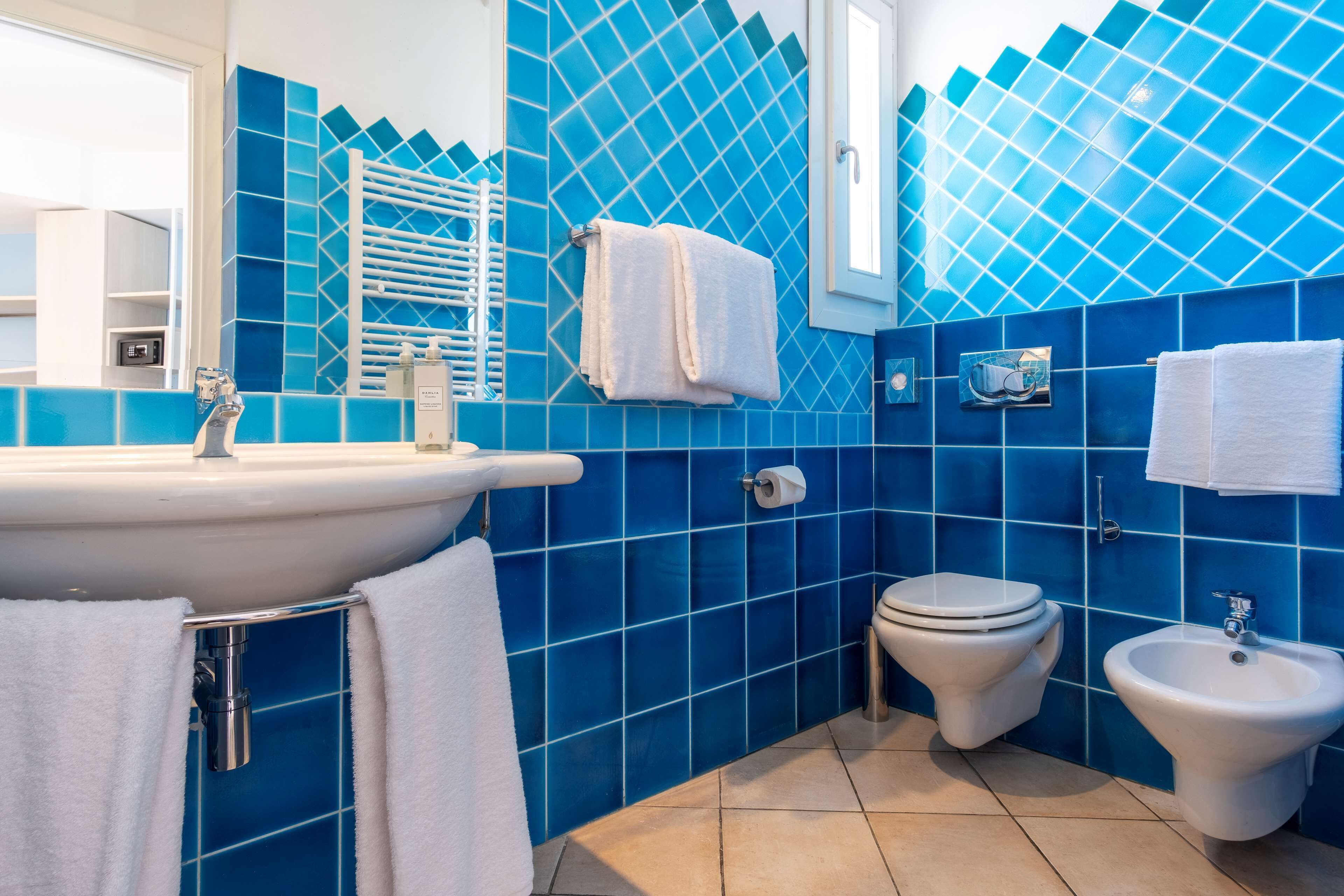 Ein Badezimmer mit Waschbecken, Toilette, Bidet und blauen Fliesenwänden.