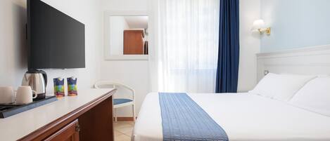 Een hotelkamer met een bed, een bureau met een televisie, een stoel en een raam met gordijnen.
