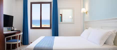 A hotel room with a bed, a desk, a chair, a television, and a window with a view of the beach.