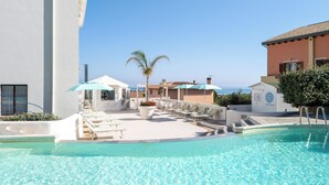 A pool area with lounge chairs and umbrellas, a palm tree, and a view of the sea. - Hotel Blumarea, BW Signature Collection (Castelsardo)
